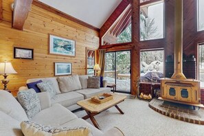 A cozy living room with a wooden interior, a sofa, a coffee table, and a wood-burning stove. - Delightful 2BR - WoodStove - Balcony - Game Room (Snoqualmie Pass)