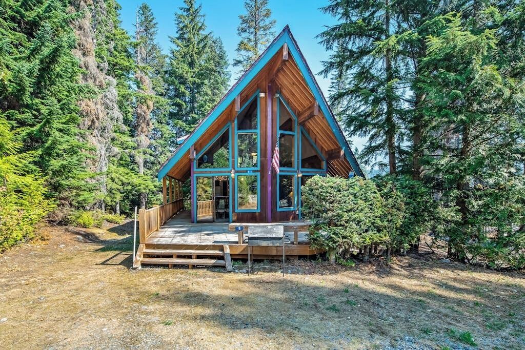 Une cabane avec un toit triangulaire, de grandes fenêtres et une terrasse en bois.