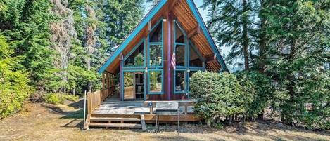 A cabin with a triangular roof, large windows, and a wooden deck.