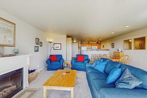 Ein Wohnzimmer mit Kamin, blauen Sofas, einem Holztisch und einer Küche im Hintergrund.