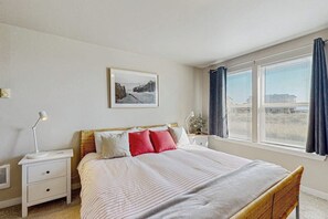Ein Schlafzimmer mit einem Bett, Nachttischen, einer Lampe, einem Bild an der Wand und einem Fenster mit Vorhängen.