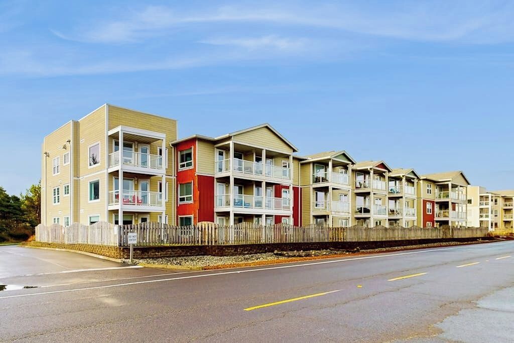 A row of multi-story residential buildings with balconies, a wooden fence, and a clear sky.