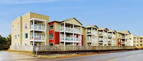 Una hilera de edificios residenciales de varios pisos con balcones, una valla de madera y cielo despejado.