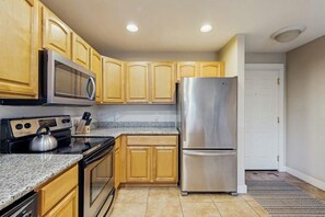 A kitchen with wooden cabinets, a stainless steel refrigerator, a microwave, and a stove. - 2BR Oceanfront 3rd-Floor - Balcony - (Westport)