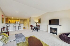 A living room with a sofa, a TV, a fireplace, and a dining area with chairs and a table. - 2BR Oceanfront 3rd-Floor - Balcony - (Westport)