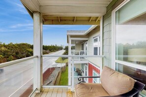 A balcony with a view of a road and greenery, a bench, and a building with large windows. - 2BR Oceanfront 3rd-Floor - Balcony - (Westport)