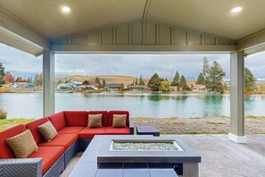 Un espace extérieur aménagé avec un canapé rouge et un foyer, offrant une vue sur un lac bordé de maisons.