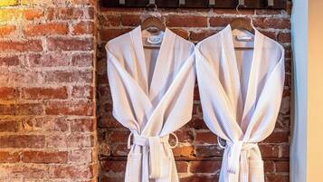 Two white bathrobes hanging on a rack against a brick wall.