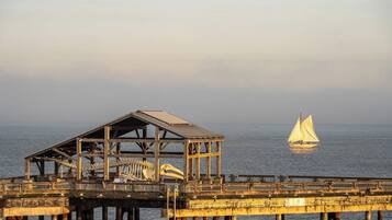 A pier with a skeletal structure and a sailboat in the distance.