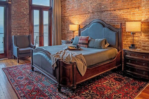 Ein Schlafzimmer mit einem großen Bett, einem Sessel, einem Nachttisch und Blick ins Freie.