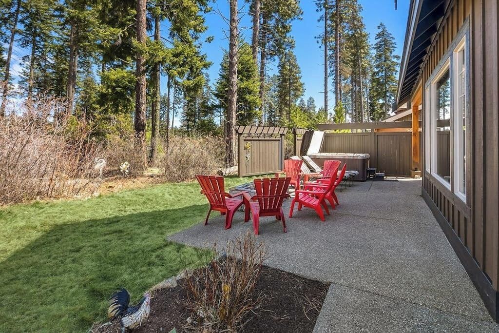 Une terrasse avec des chaises rouges et une table, entourée d’une clôture en bois et de grands arbres.