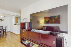 A modern living room with a wooden cabinet, a flat-screen TV, and a colorful abstract painting on the wall. - 1BR condo near attractions with pool & hot tub (Seattle)