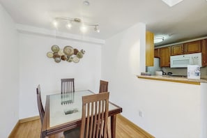 A dining area with a glass table and wooden chairs, a wall-mounted decorative plate arrangement, and a kitchen with wooden cabinets and a microwave. - 1BR condo near attractions with pool & hot tub (Seattle)