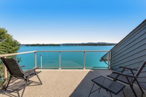 A balcony with a clear view of a lake, two chairs, and a table.