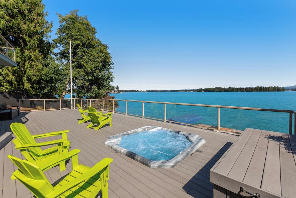 Una terraza de madera con un jacuzzi y sillas verdes que da a una masa de agua.