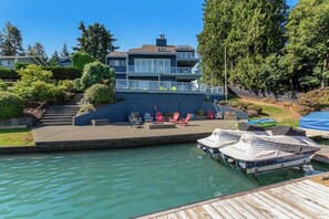A waterfront property with a dock, a covered boat, and a patio area with chairs.