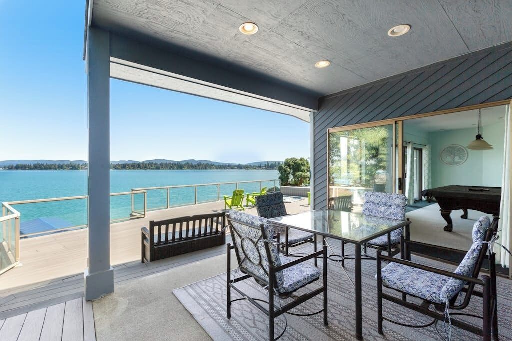 Une terrasse extérieure avec une table et des chaises en verre, donnant sur une étendue d’eau.