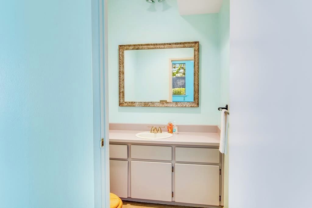 Een badkamer met een lichtblauwe wand, een wit wastafelmeubel en een spiegel met houten lijst.