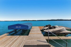 A wooden dock leading to a boat with a blue cover labeled 'AQUA LIFT' and a jet ski on the right.