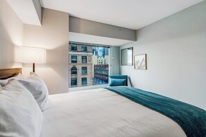 A hotel room with a large bed, a view of buildings through a window, a chair, and a lamp. - 2 BR downtown condo with amazing views & pool (Seattle)