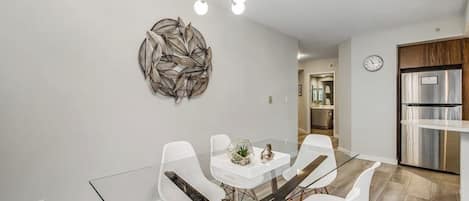 Un comedor moderno con una mesa de vidrio, sillas blancas y un adorno en la pared.