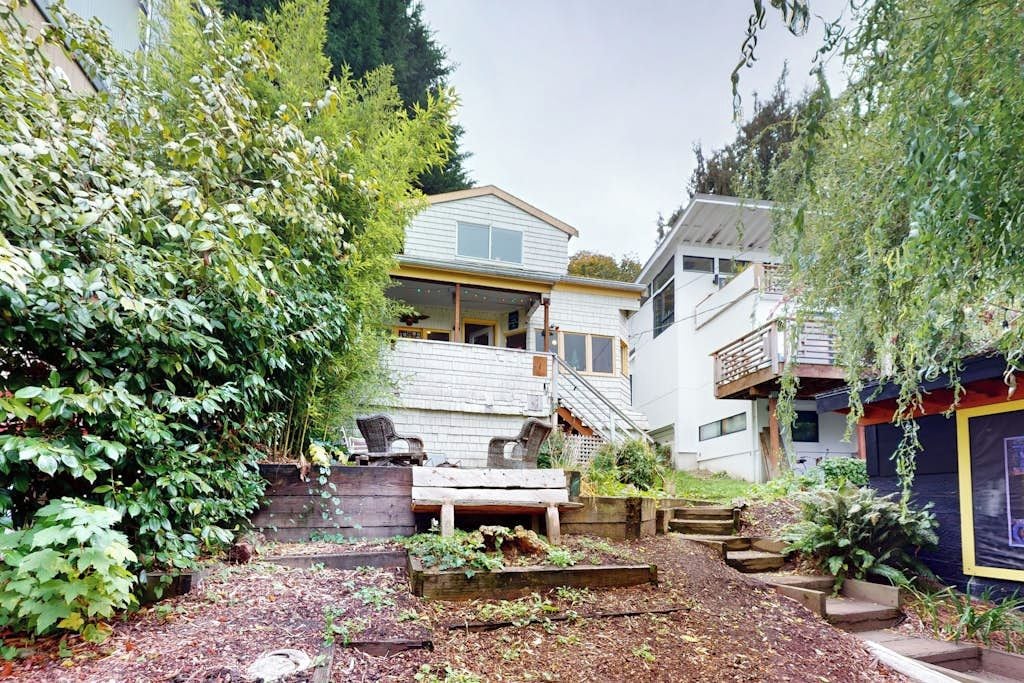 A residential property with a multi-level house, a deck, and a garden area with plants and steps.