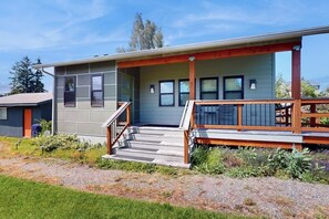 A modern two-story house with a covered porch and a staircase leading to the entrance. - Designer Cottage | Accessible Kitchen & Bathroom (Tacoma)