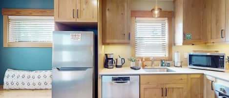 Una cocina compacta con armarios de madera, refrigerador de acero inoxidable, microondas, lavavajillas y una ventana con persianas.