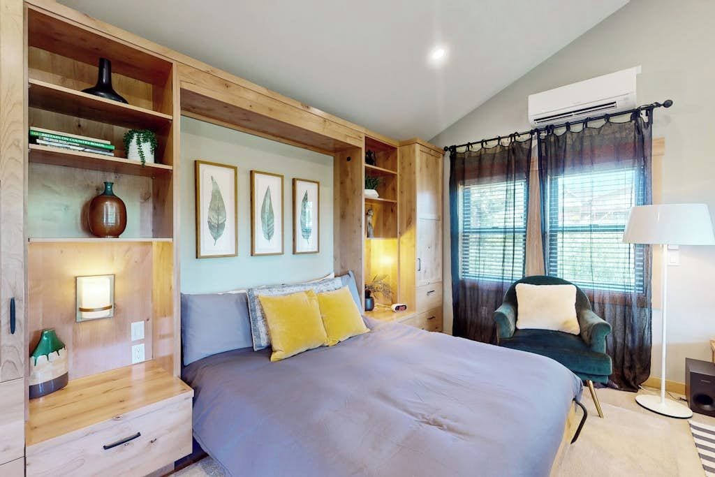 A bedroom with a large bed, wooden shelving, a desk, a chair, and a window with curtains.