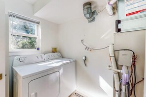Ein Waschraum mit einer Frontlader-Waschmaschine und einem Trockner, einem Fenster mit Jalousien sowie einem Wandheizkörper.