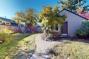 A residential backyard with a paved walkway, a wooden fence, and a house with a dark door. - Elegant 3BR Dog Friendly - Patio - Pool Table (Seattle)