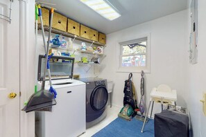 A laundry room with a washing machine, shelves with cleaning supplies, a vacuum cleaner, and a window. - Elegant 3BR Dog Friendly - Patio - Pool Table (Seattle)