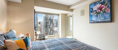 Un dormitorio con una cama grande, vistas de la ciudad a través de una ventana y un cuadro en la pared.