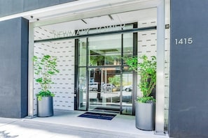 A modern building entrance with a glass door, a metal sign above the door, and two potted plants on either side. - 2BR modern home with amazing views, pool & hot tub (Seattle)