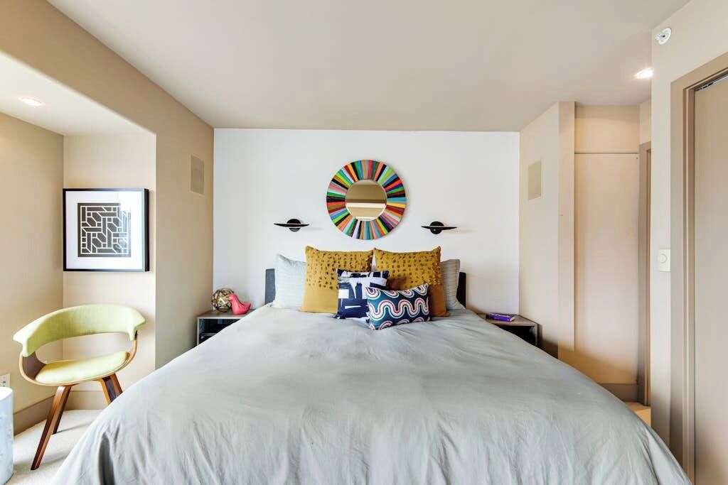 A modern bedroom with a large bed, a wall-mounted circular artwork, and a chair.