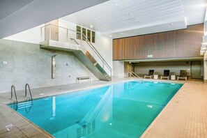 Une piscine intérieure avec un escalier menant à un balcon, des chaises longues et un mur revêtu de panneaux en bois.