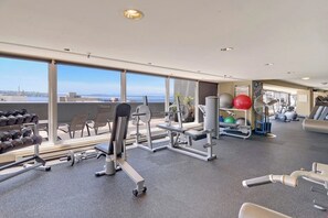 A gym with various exercise equipment, large windows, and a view of the city. - Luxury 2BR Bayview Washington State Conv. Center 2 (Seattle)