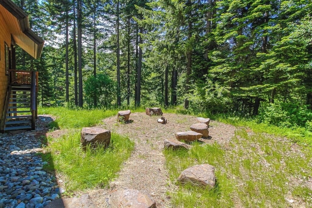 A wooden cabin with a stone pathway leading to a seating area surrounded by trees.
