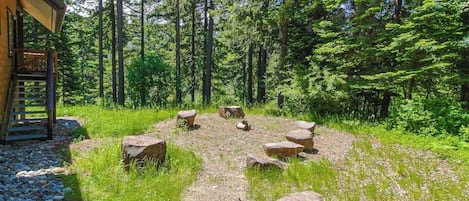 Une cabane en bois avec un chemin de pierres menant à un espace aménagé pour s’asseoir, entouré d’arbres.