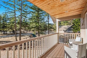 Eine Holzterrasse mit Geländer, mit Blick auf eine bewaldete Landschaft unter blauem Himmel.