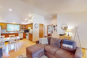 Ein modernes Wohnzimmer mit einem braunen Sofa, einem Esstisch mit Stühlen und einer Küchenzeile mit Holzausbau und einer Mikrowelle.