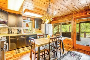 Een houten interieur met een keuken, eethoek en grote ramen.