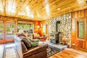 A wooden interior with a stone fireplace, leather sofa, and a dining area. - Quiet 2BR riverfront cabin with wood stove (Cle Elum)