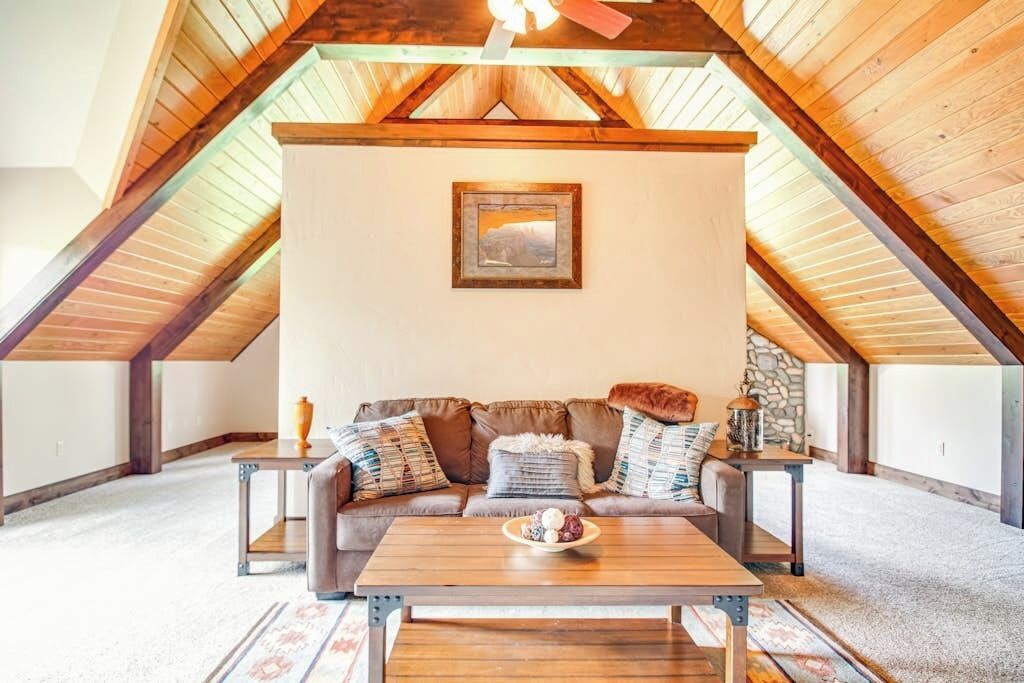 An attic room with a wooden ceiling, a sofa set, a coffee table, and a framed picture on the wall.