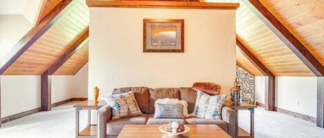 An attic room with a wooden ceiling, a sofa set, a coffee table, and a framed picture on the wall.