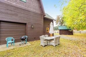 Een houten schuur met een overdekt terras, een barbecue en een kleine tuinhuis.