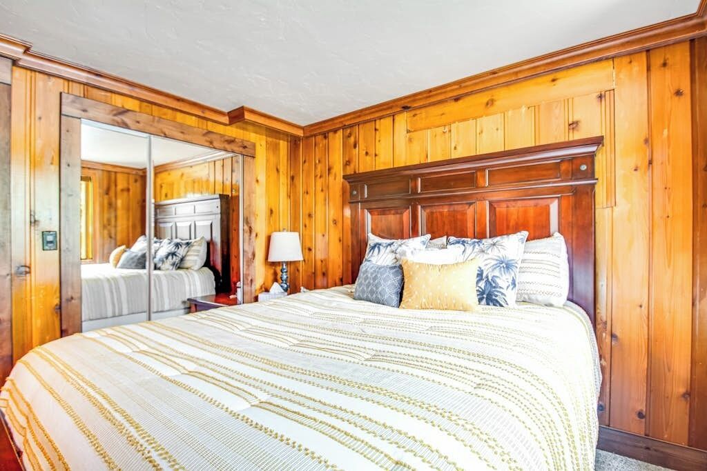 A bedroom with a wooden paneled wall, a large bed with a striped bedspread, and a nightstand with a lamp.