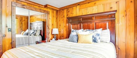 A bedroom with a wooden paneled wall, a large bed with a striped bedspread, and a nightstand with a lamp.