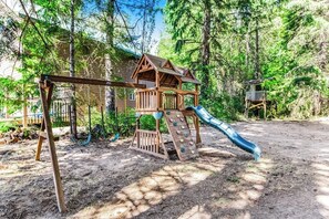 A wooden play structure with a slide and climbing wall in a forested area. - 2BR lakefront cabin with private dock (Cle Elum)