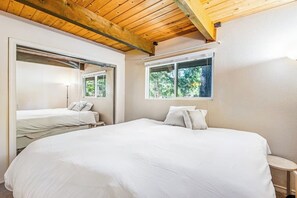 A bedroom with a large bed, a smaller bed, a window with a view of trees, and a wooden ceiling. - 2BR lakefront cabin with private dock (Cle Elum)